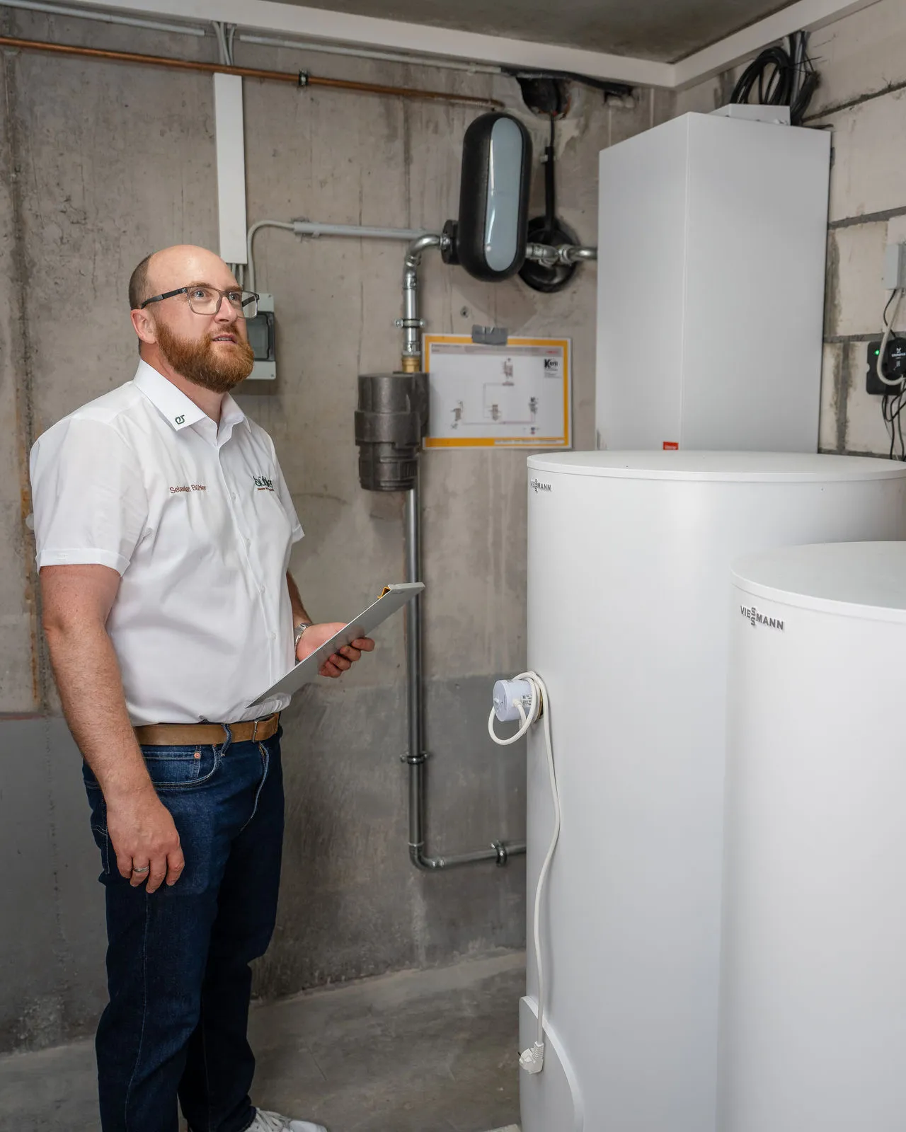 Energieberater mit Tablet vor Wärmepumpenanlage in Gebäudekeller