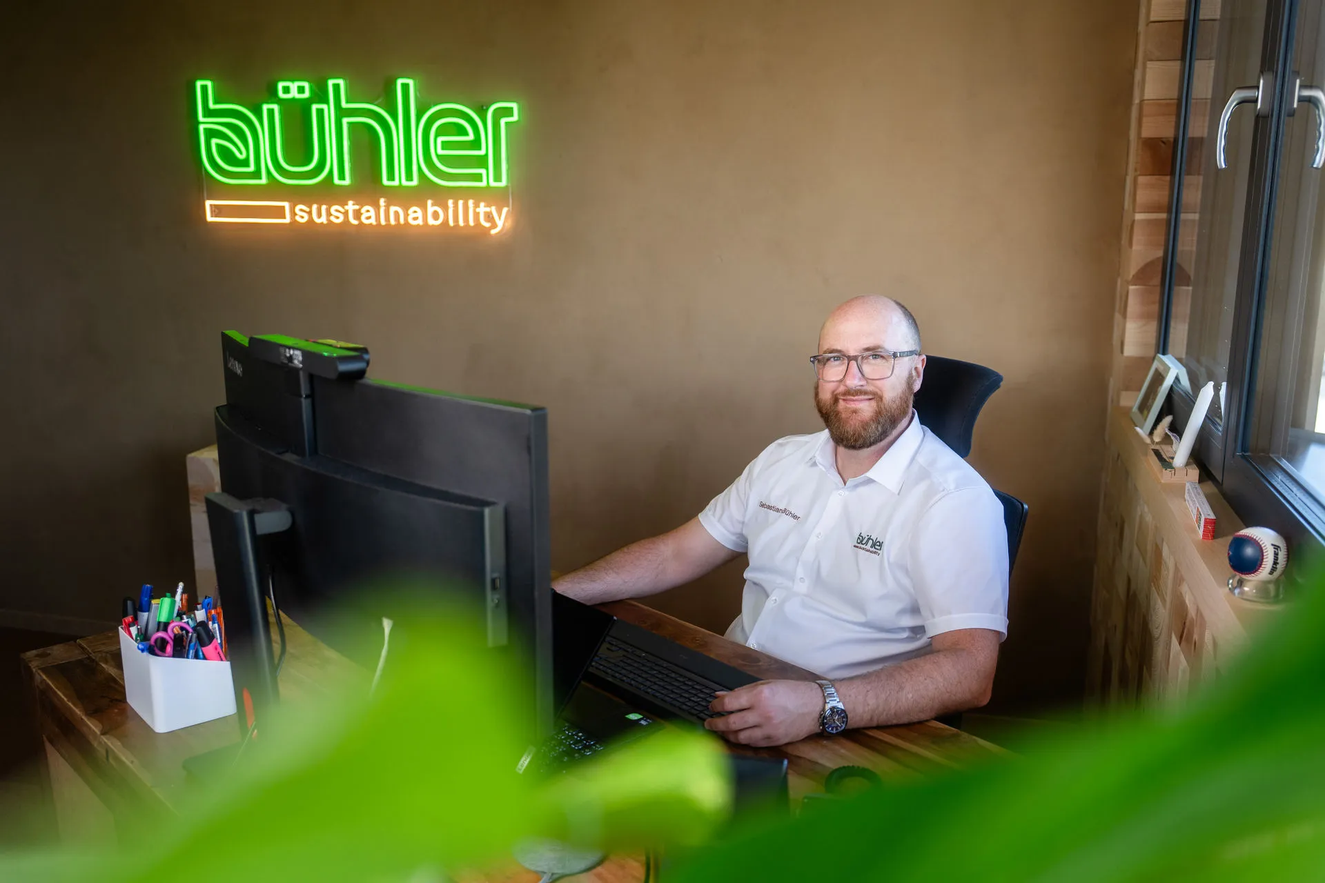 Sebastian Bühler in seinem Büro mit Neon-Logo bühler sustainability